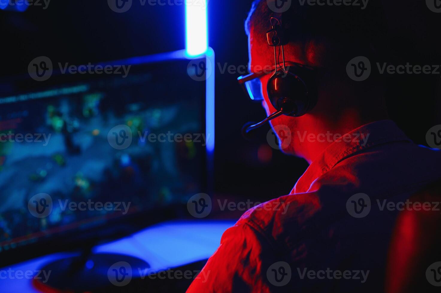 Professional Gamer Plays Game on His Computer. He's Participating in Online Cyber Games Tournament or in Internet Cafe. He Wears Glasses and Talks into Microphone. photo