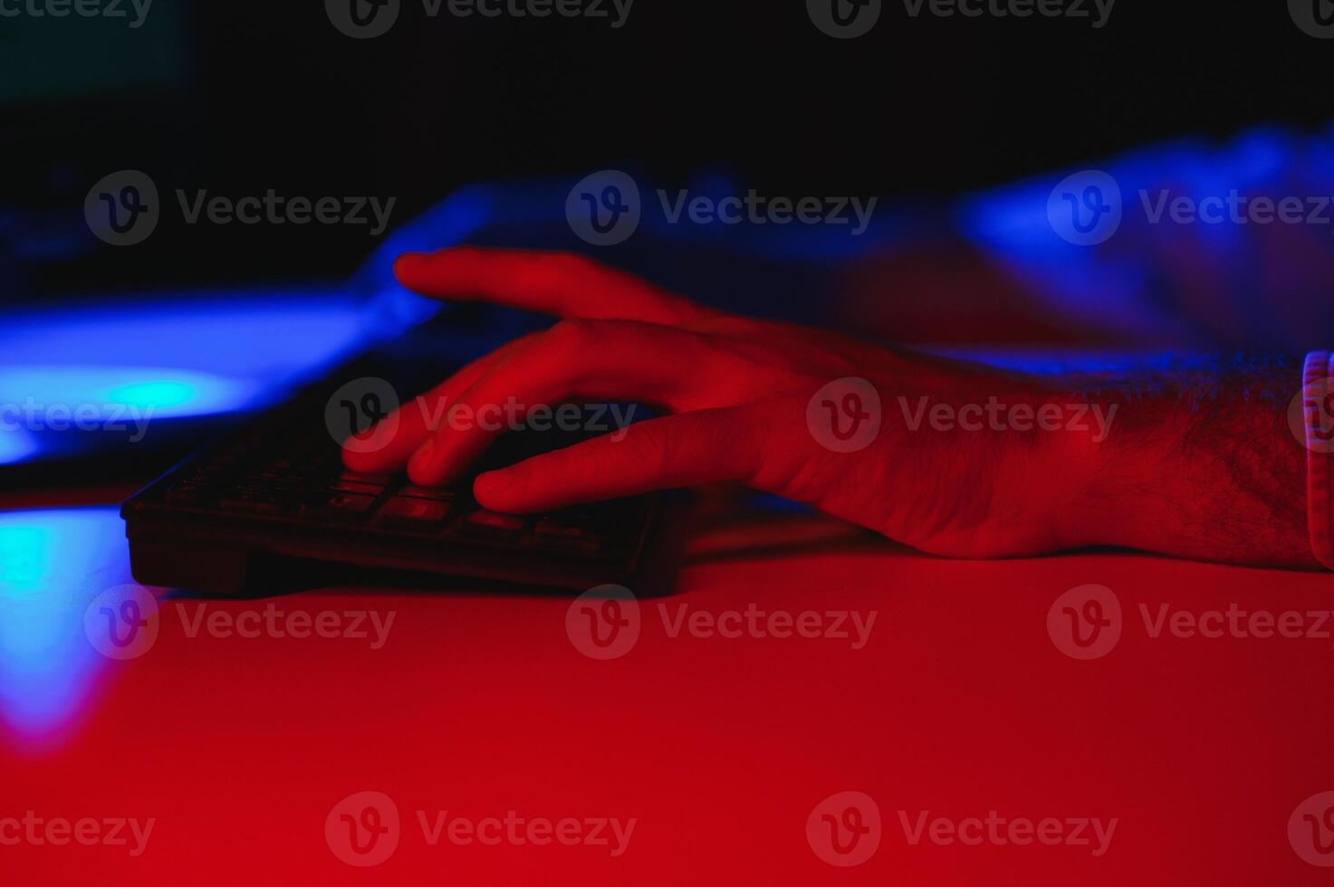 Close-up On Gamer's Hands on a keyboard, Actively Pushing Buttons, Playing MMO Games Online. Background is Lit with Neon Lights. photo