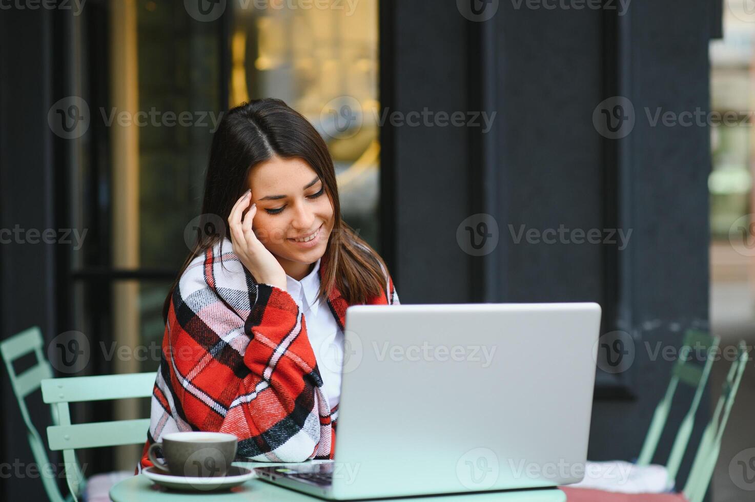 Young, a girl in an outdoor cafe with a laptop talking through a call with someone, Aipi telephony photo