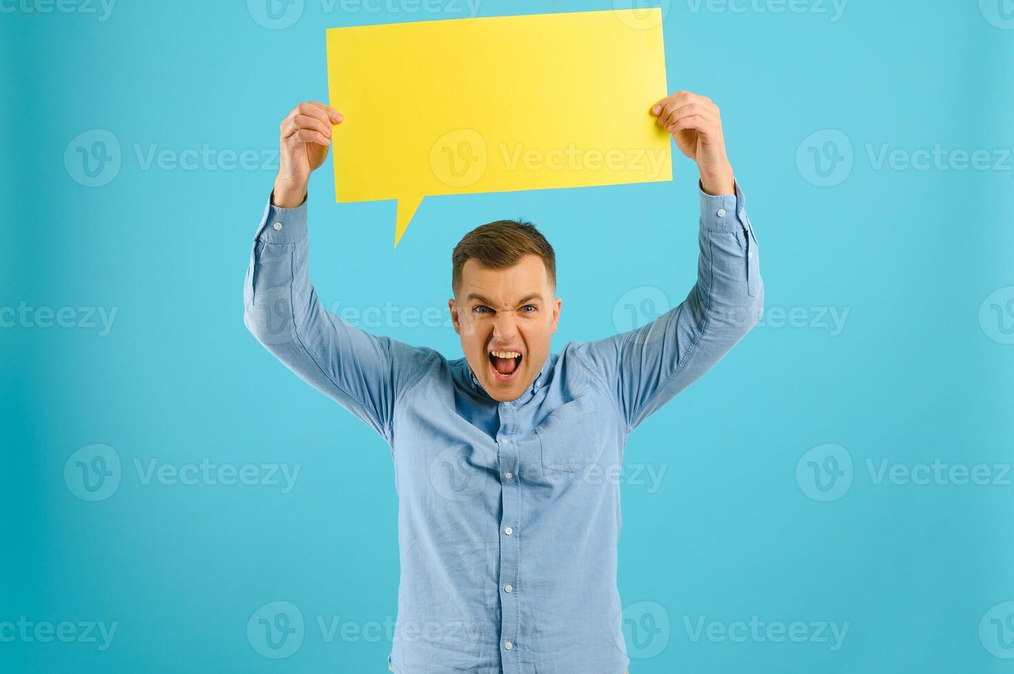 Handsome smiling man holding blank speech bubble sign isolated on light blue studio banner background with copy space photo