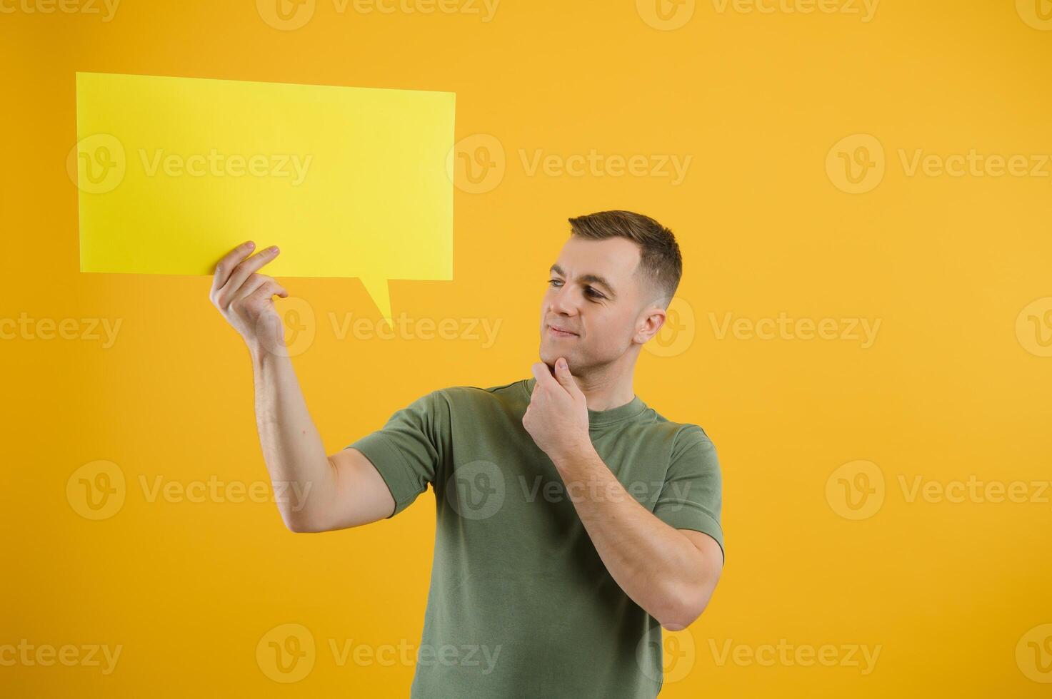 Happy guy smiling and holding blank speech balloon near head against yellow background photo