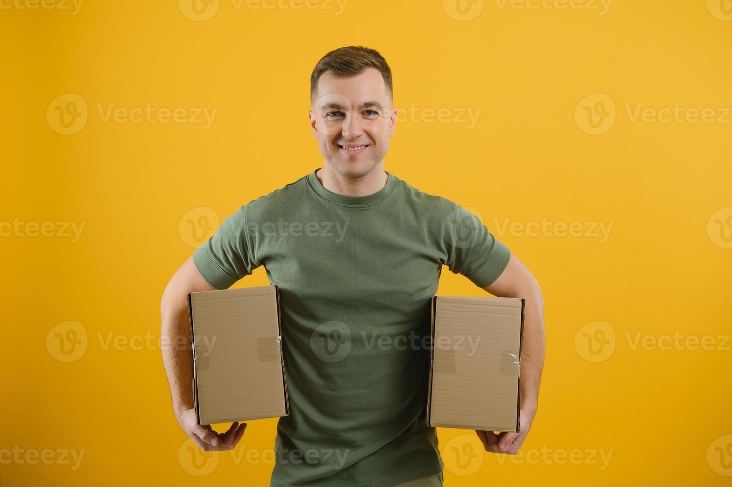 Cute man holding a cardboard box on a yellow background. Delivery service concept. Free space for advertising. photo