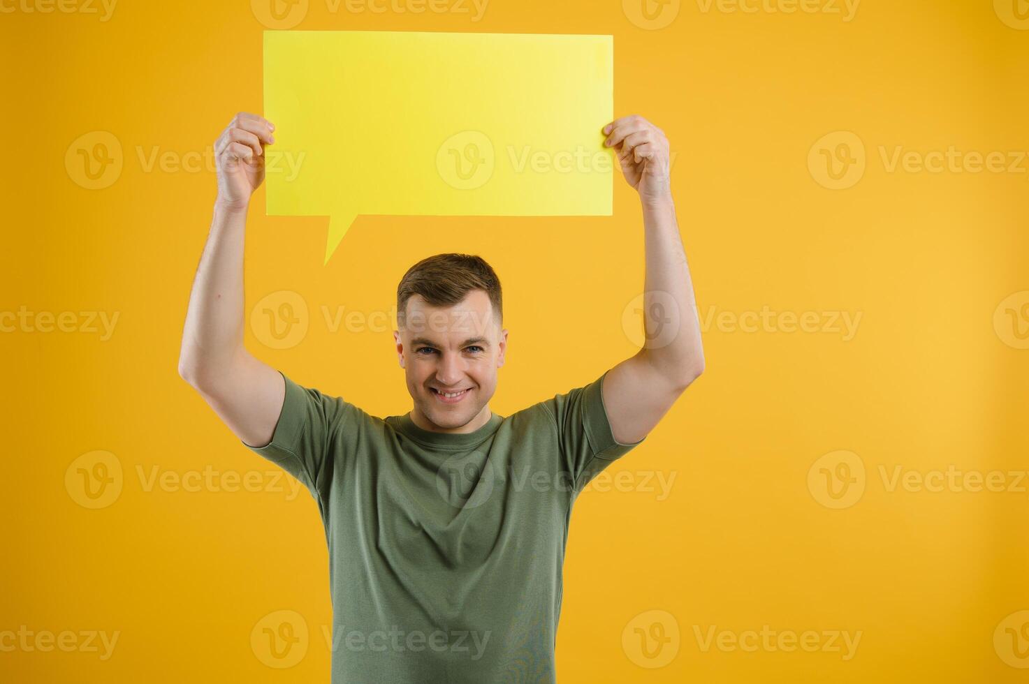 Cheerful young male pointing up and holding empty speech bubble with blank space for quote against vivid yellow background photo