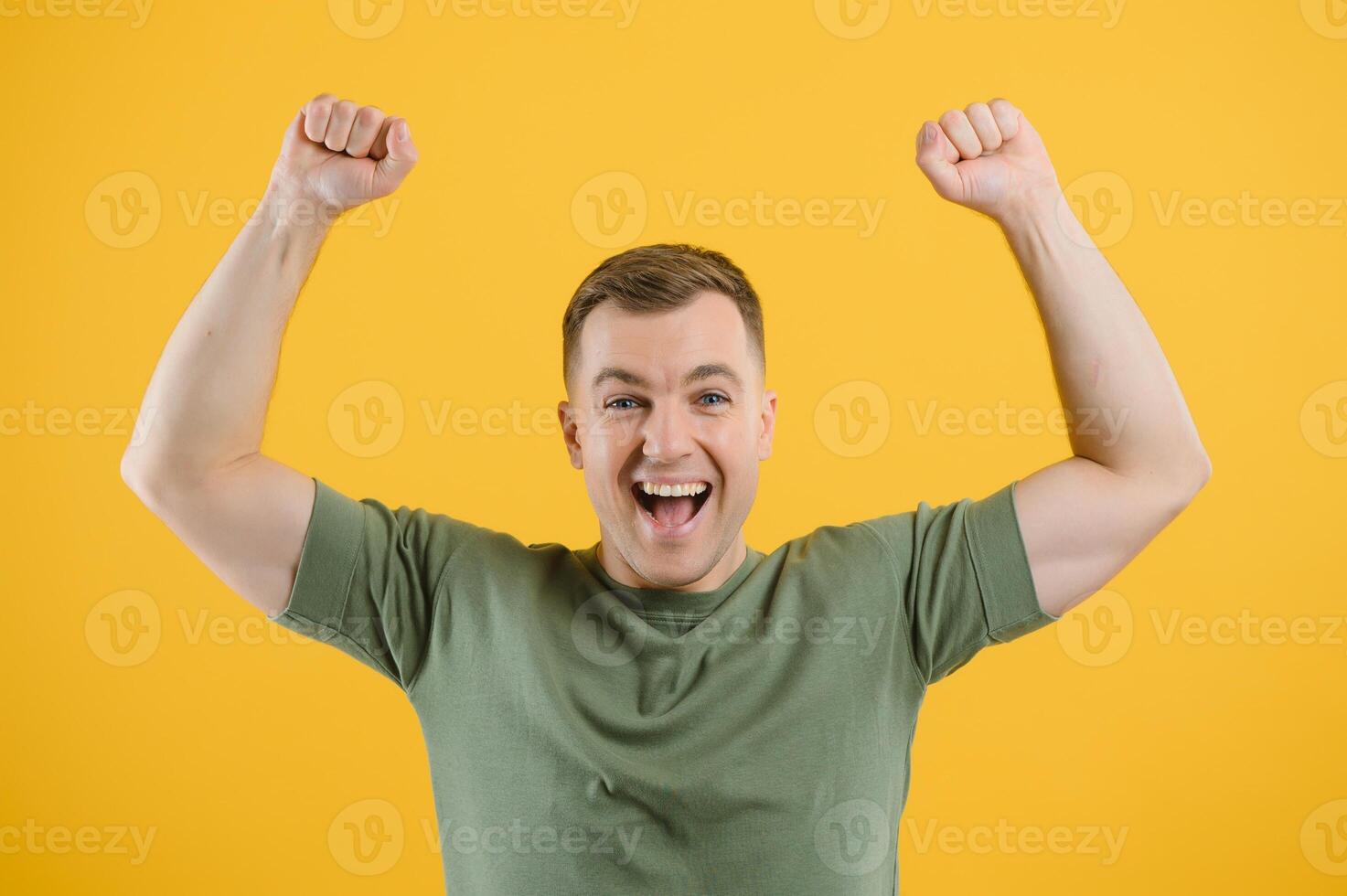 Excited young man guy posing isolated on yellow background studio portrait. People lifestyle concept. Mock up copy space. Rising hands, clenching fists like winner photo