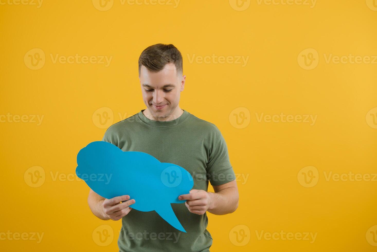 Cheerful young male pointing up and holding empty speech bubble with blank space for quote against vivid yellow background photo