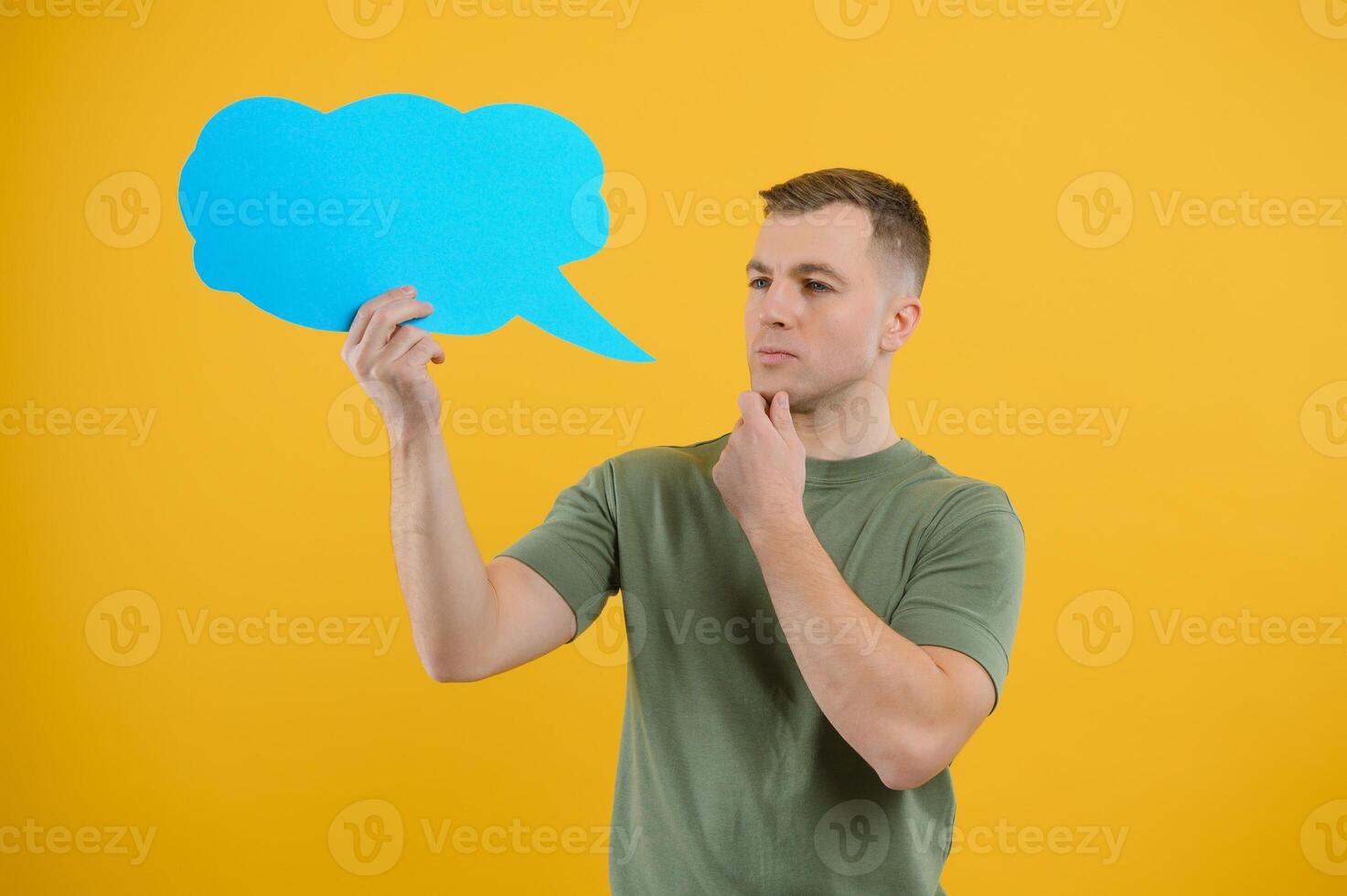 Cheerful young male pointing up and holding empty speech bubble with blank space for quote against vivid yellow background photo