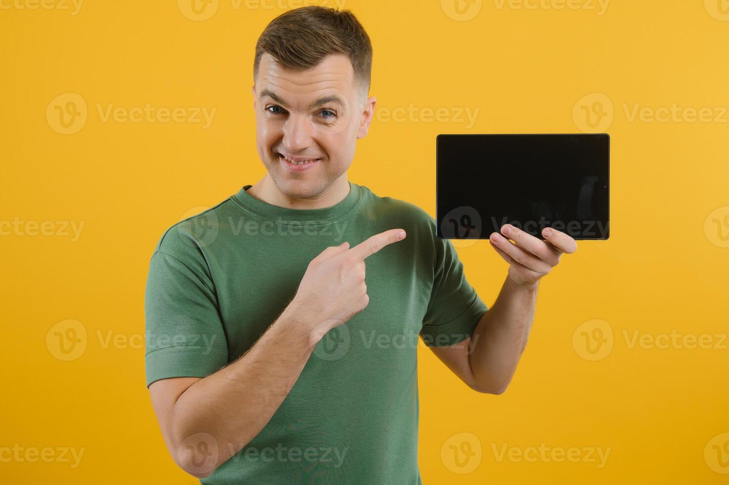 Amazed happy man using digital tablet looking shocked about social media news, astonished man shopper consumer surprised excited by online win isolated over yellow background. photo
