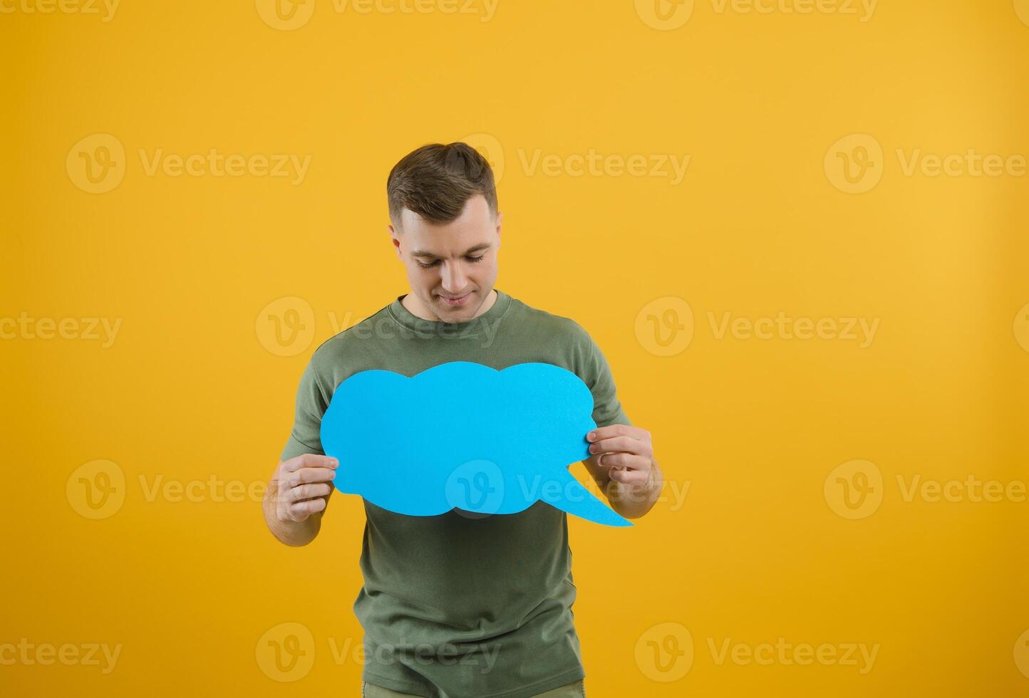 Cheerful young male pointing up and holding empty speech bubble with blank space for quote against vivid yellow background photo