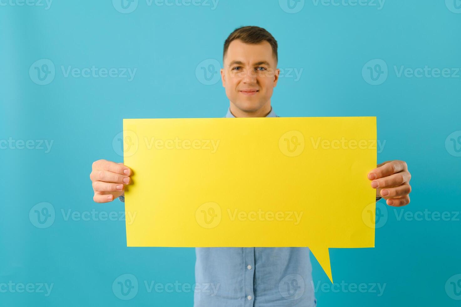 Joyful Caucasian man demonstrating blank placard on blue studio background, mockup for design photo