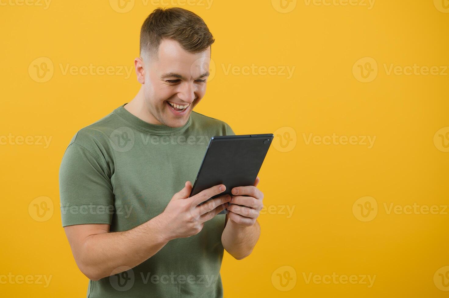 Amazed happy man using digital tablet looking shocked about social media news, astonished man shopper consumer surprised excited by online win isolated over yellow background. photo