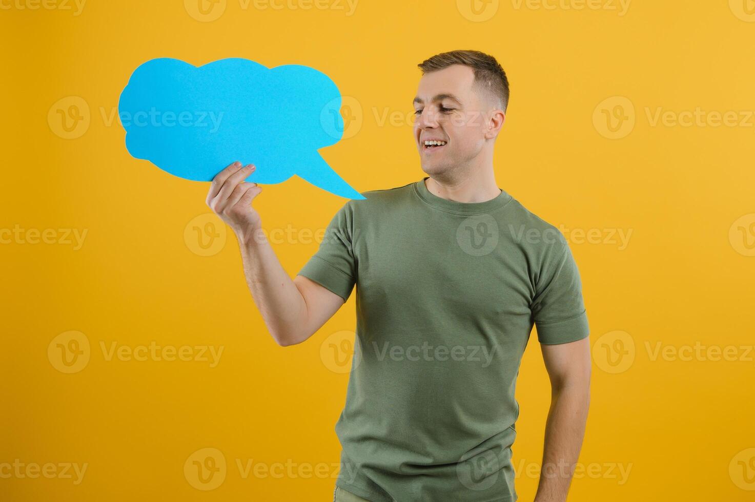 Cheerful young male pointing up and holding empty speech bubble with blank space for quote against vivid yellow background photo
