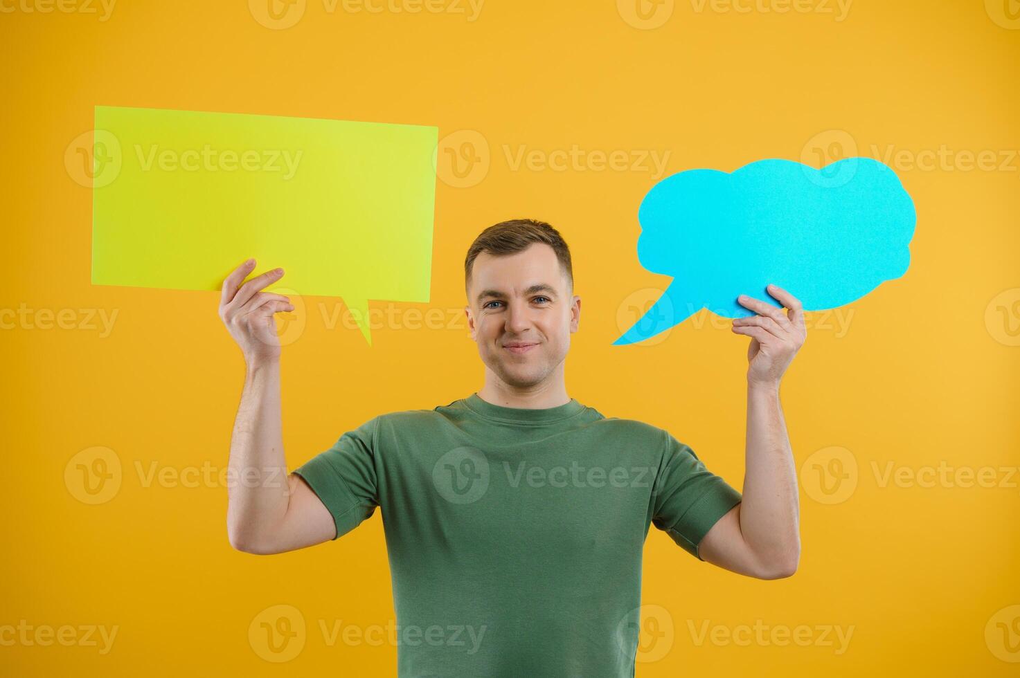 Portrait of cheerful smiling young handsome man holding and looking up at speech bubble with empty space for text on colorful yellow studio background photo