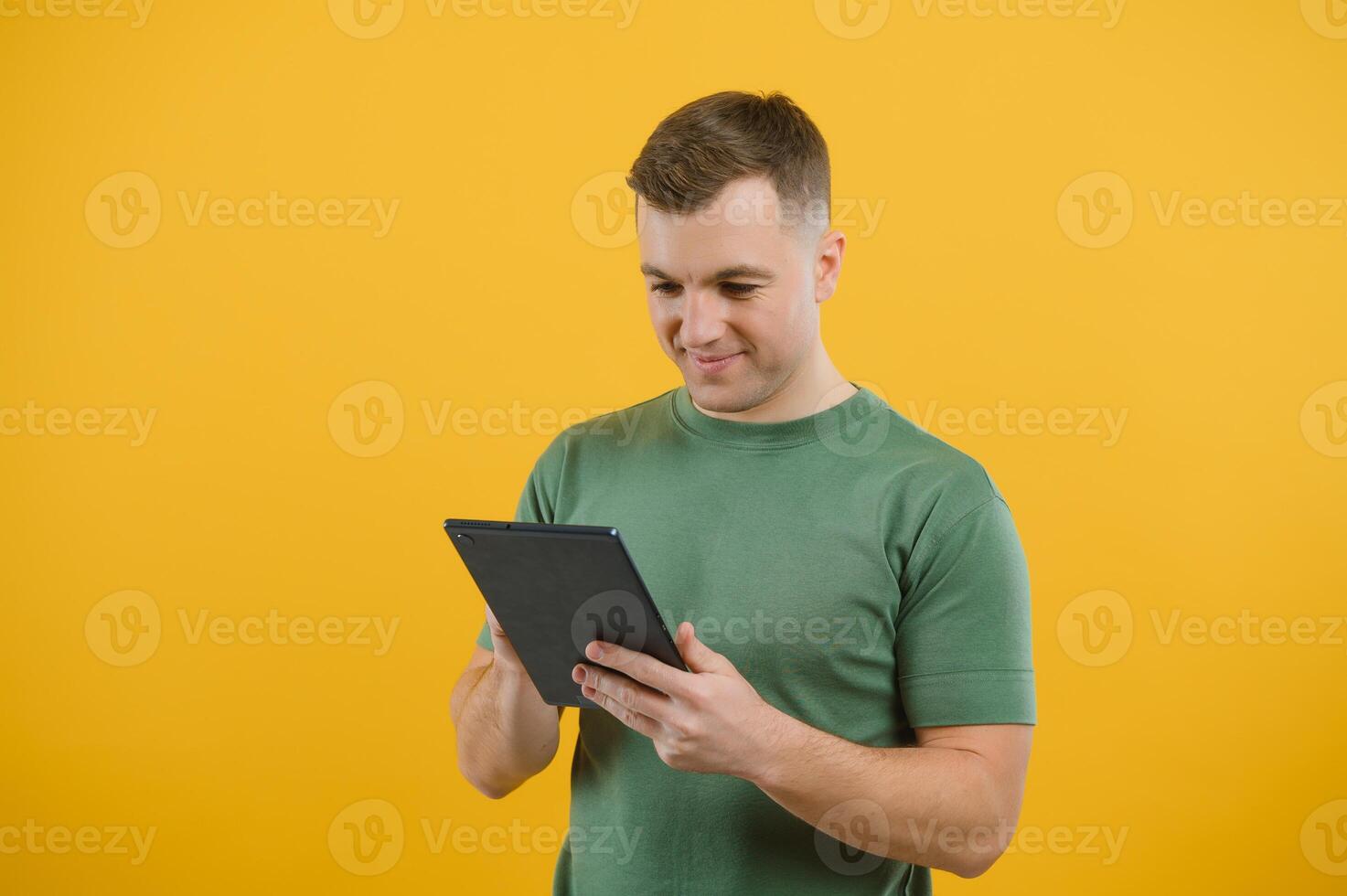 Amazed happy man using digital tablet looking shocked about social media news, astonished man shopper consumer surprised excited by online win isolated over yellow background. photo