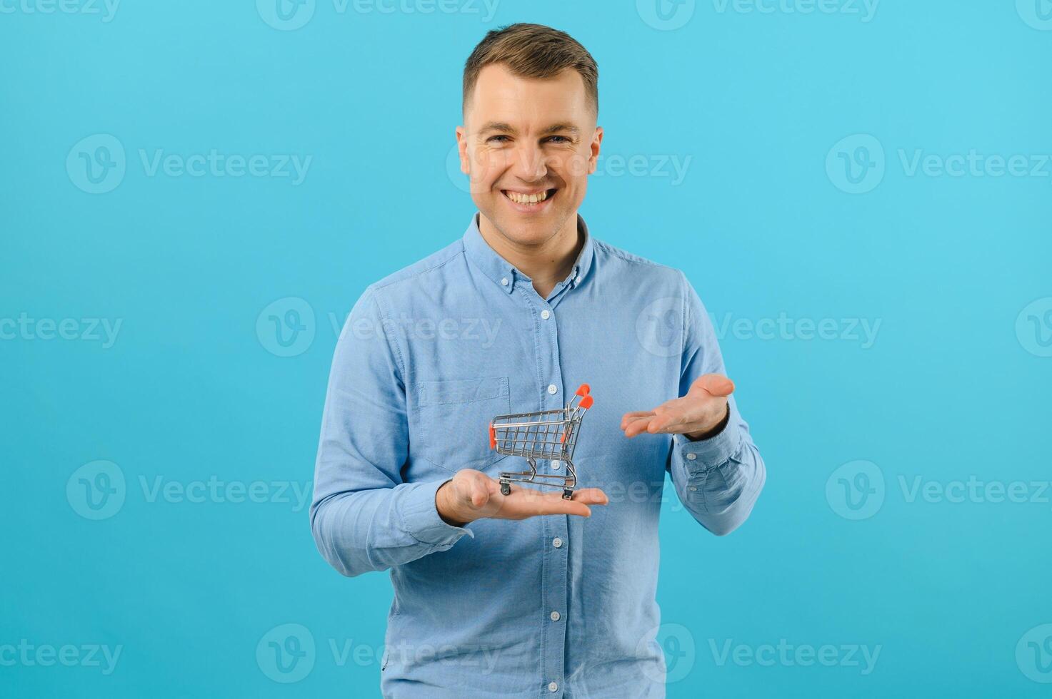 Portrait of smiling man holding mini shopping baskets on blue background. The concept of increasing sales. photo
