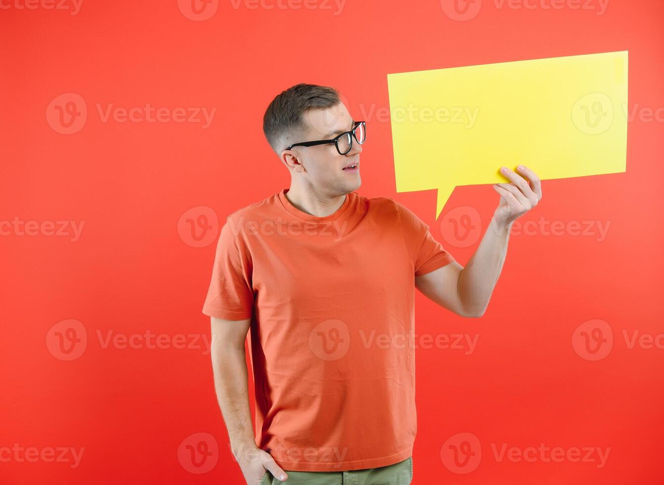 Happy smiling man holding yellow bubble speech, looking at camera over red background photo