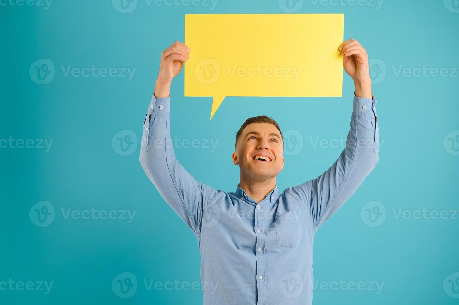 Handsome smiling man holding blank speech bubble sign isolated on light blue studio banner background with copy space photo