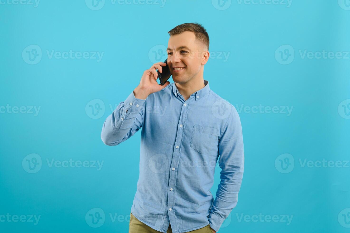 Young caucasian handsome man isolated on blue background looking at the camera and smiling while using the mobile photo