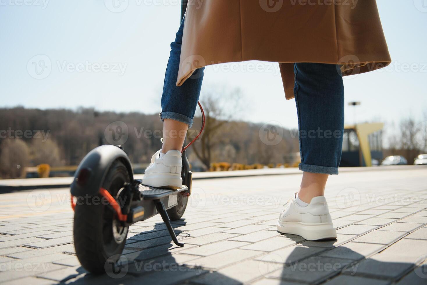 Close up of woman riding black electric kick scooter at cityscape, motion blur photo