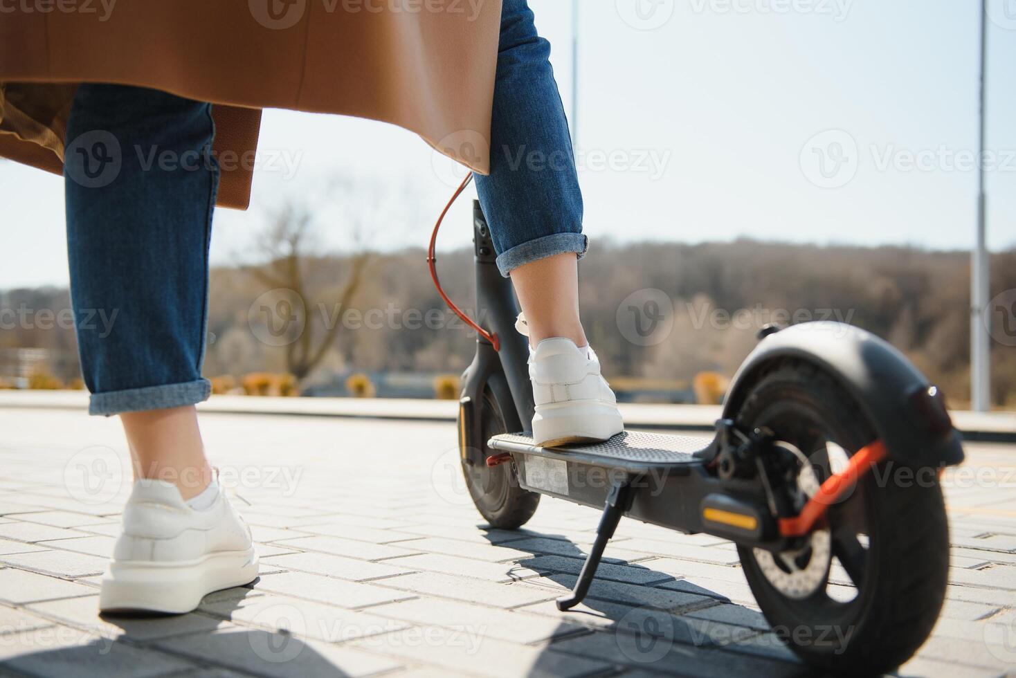 Close up of woman riding black electric kick scooter at cityscape, motion blur photo