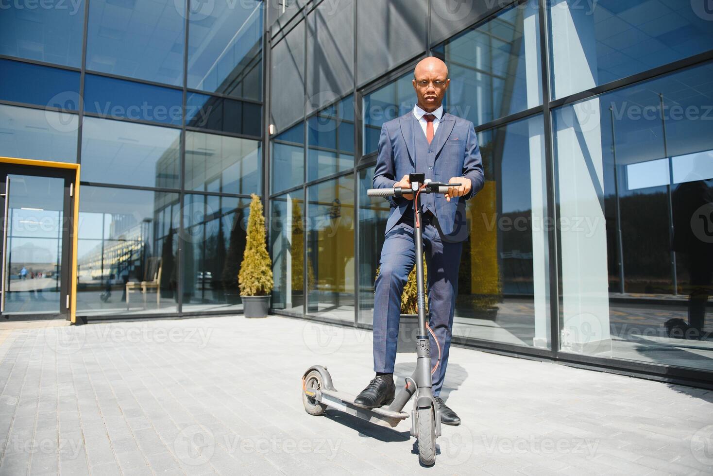 businessman with electric scooter standing in front of modern business building talking on phone. photo