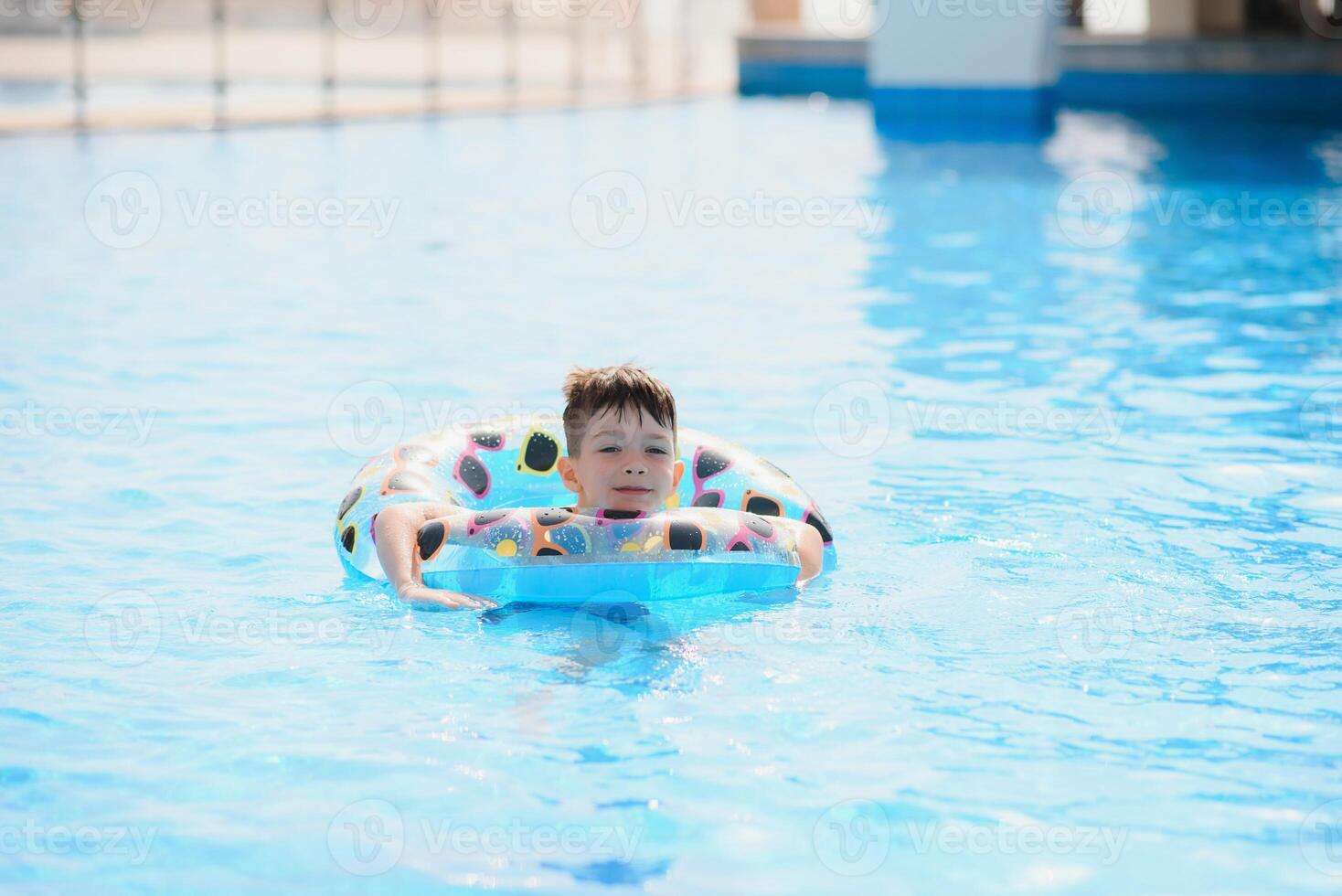 Happy boy in swimming pool. Boy is alone, swimming inflatable ring and surronded by water splashes. Wet teenager is enjoying summer weekend in amusement water park. Banner with copy space photo