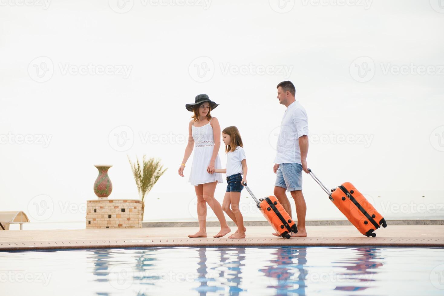 young family with suitcases walking to hotel building with beautiful swimming pool. traveling and relaxing time concept. photo