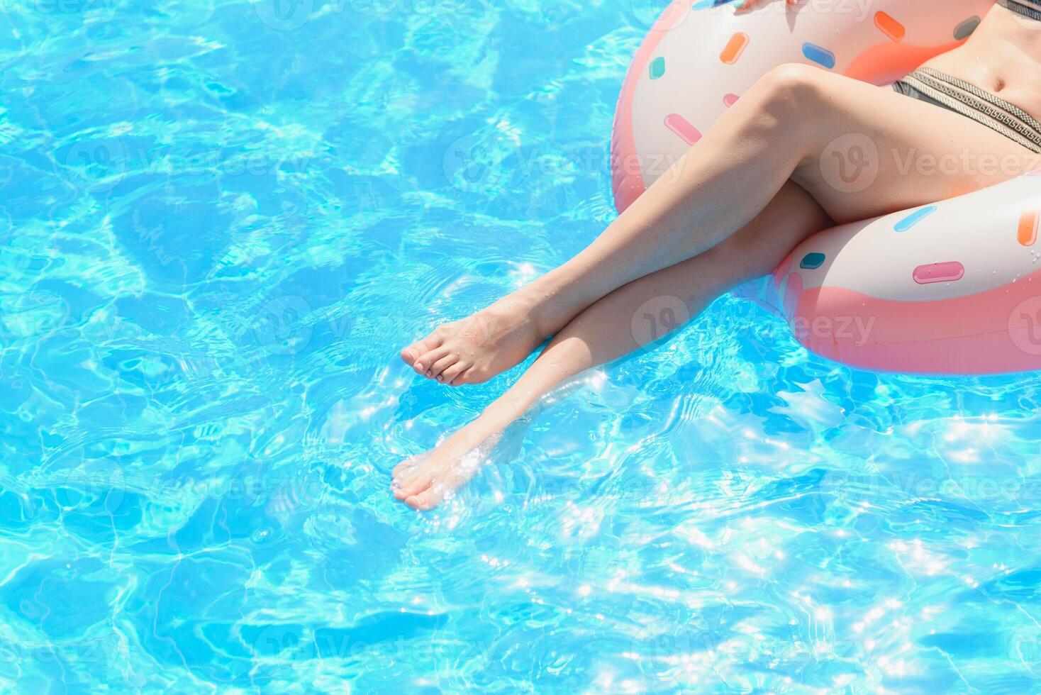 Beautiful young woman with inflatable donut in blue swimming pool photo