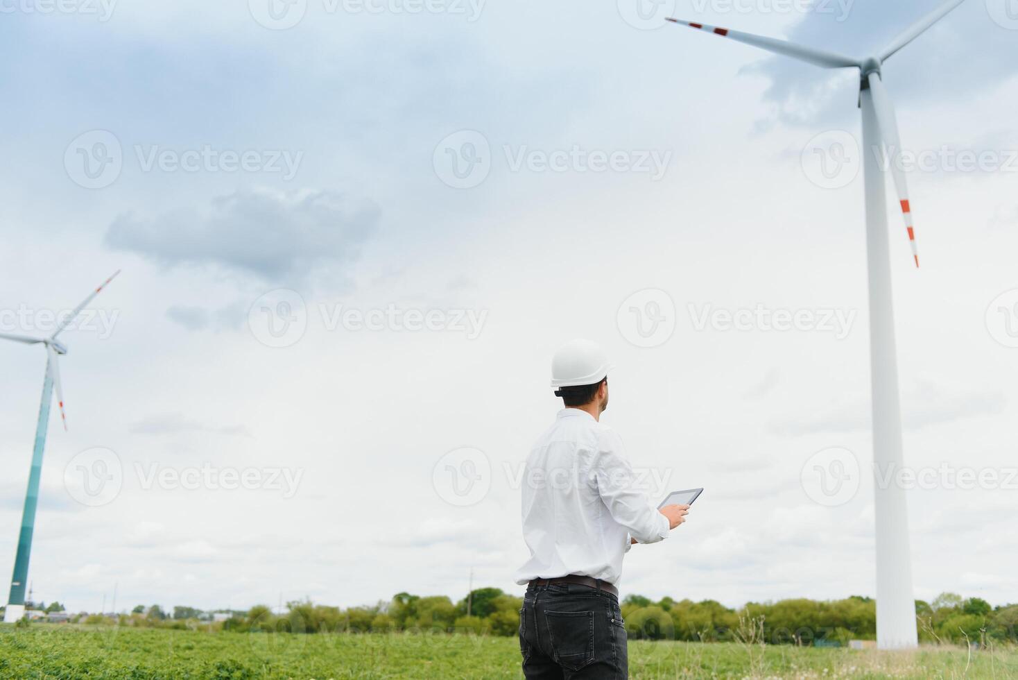 Engineer is checking energy production on wind turbine. Worker in windmills park in helmet and with tablet. photo