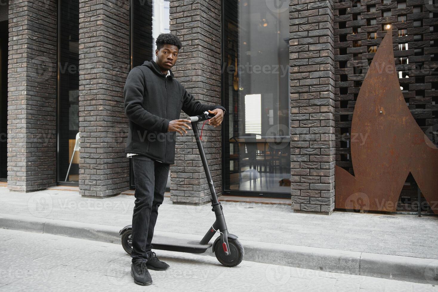afro american guy rides an electric scooter against the background of a wall, a student uses eco transport photo
