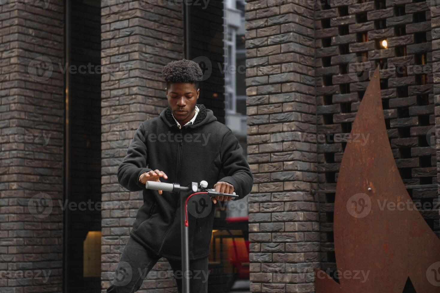 Active Leisure Concept. Side view of black male student driving stand-up scooter over brick road, copy space for ad or text photo
