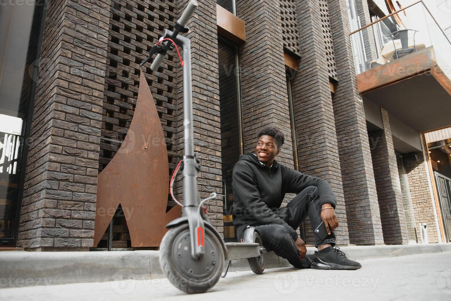afro american guy rides an electric scooter against the background of a wall, a student uses eco transport photo