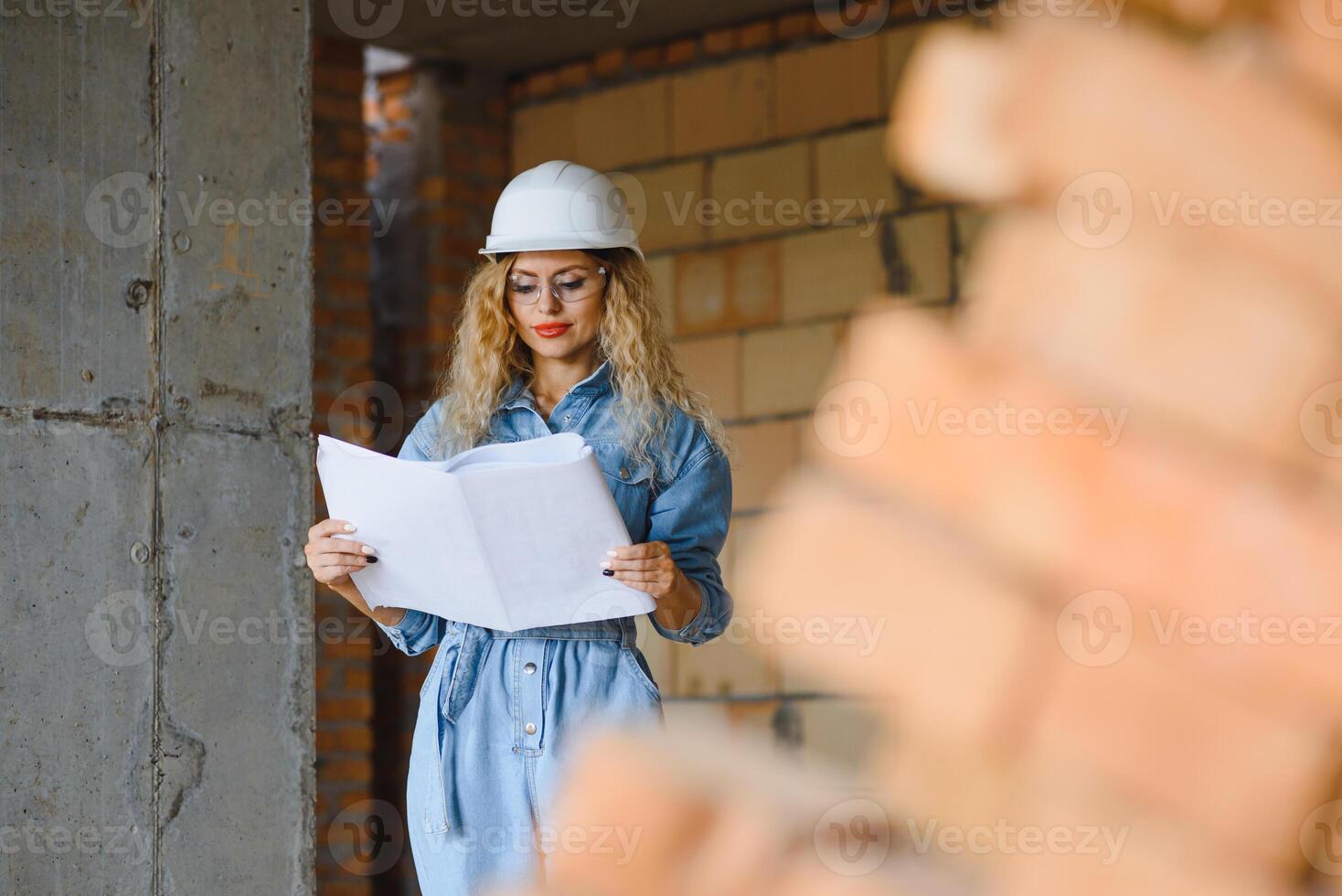 Construction concept. Pretty female builder in overalls and helmet working on construction site. photo
