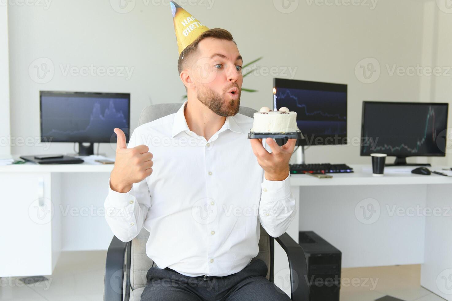 Young happy businessman celebrating his birthday in the office. He holds a cake in his hands. photo