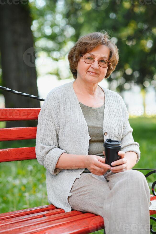 Elderly woman sitting and relaxing on a bench outdoors in park photo