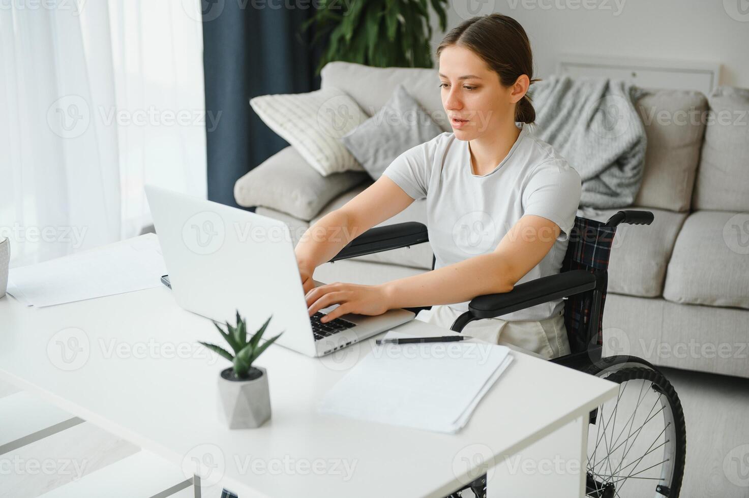 Freelancer in wheelchair using laptop near notebook and papers on table photo