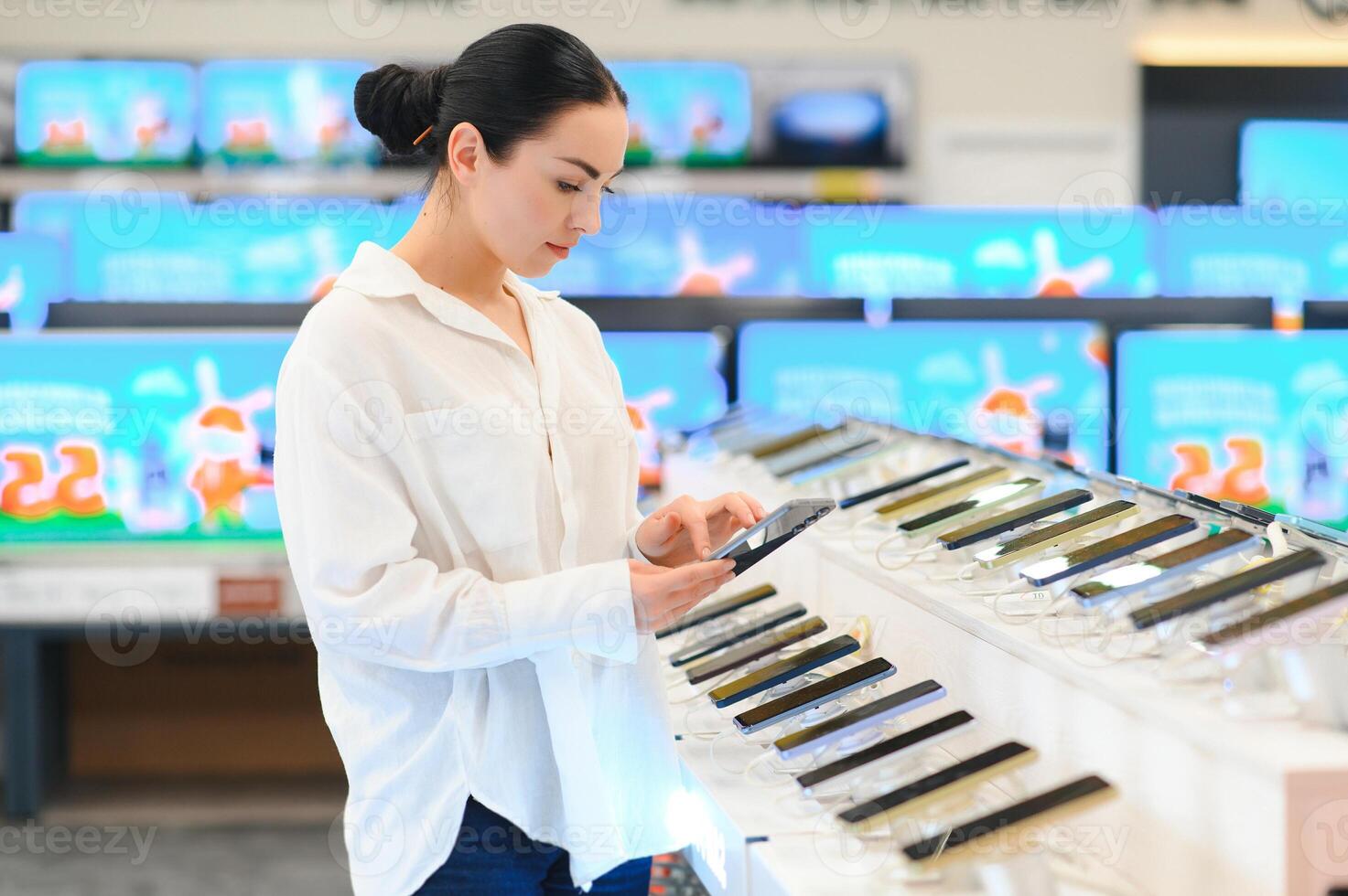 Portrait of happy young woman buying a new smartphone in store. Shopping a new digital device photo
