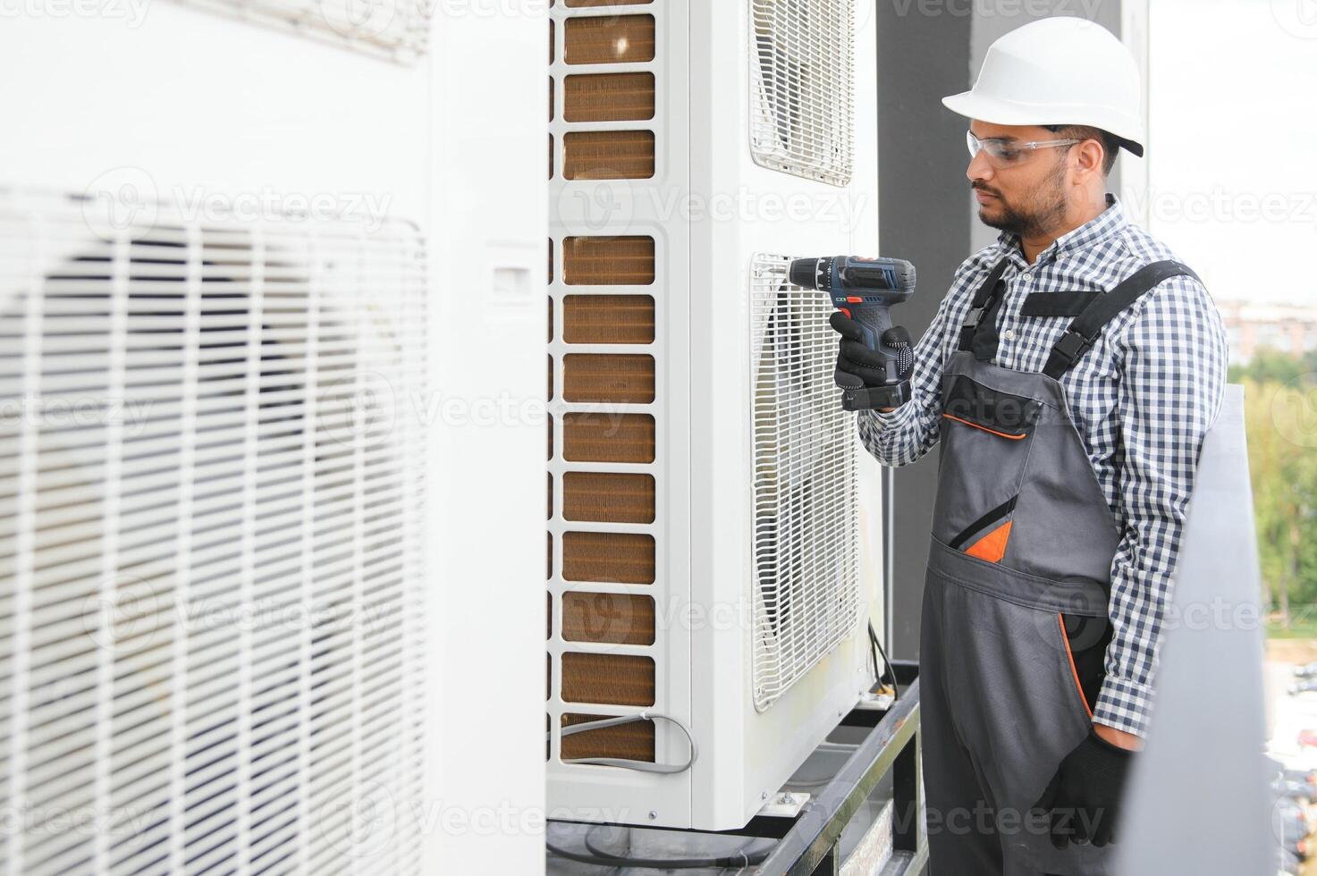 Young indian man repairman checking an outside air conditioner unit photo