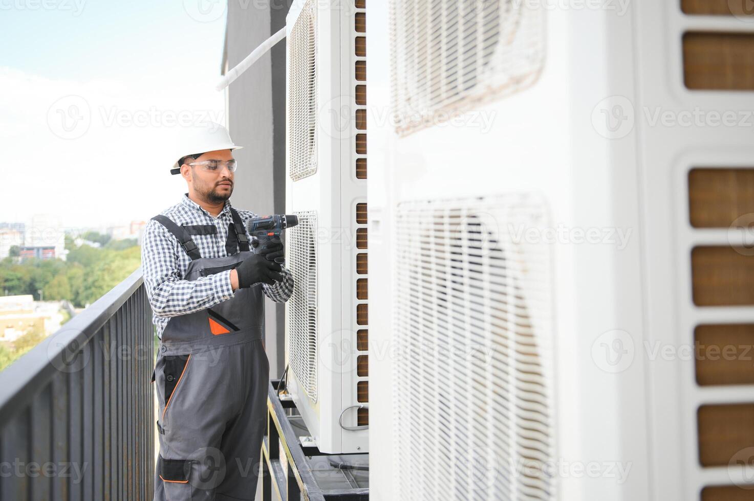 Young indian man repairman checking an outside air conditioner unit photo
