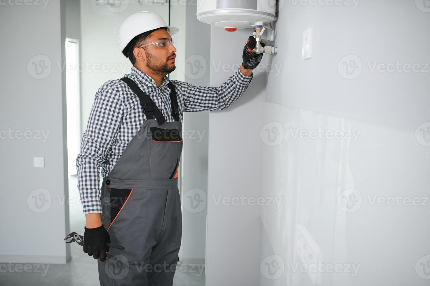 Indian plumber using screwdriver while fixing boiler or water heater, working on heating system in apartment photo