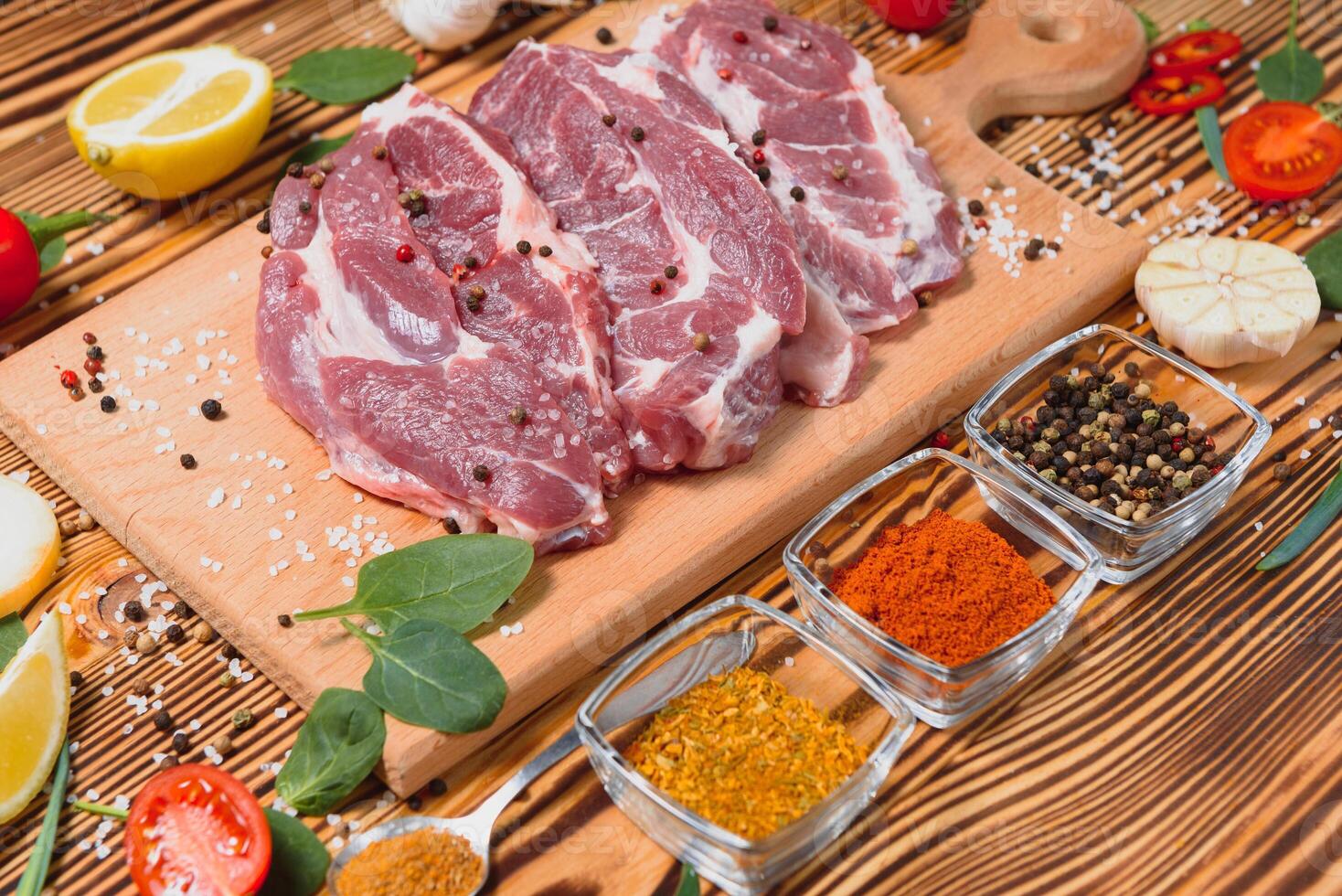 Raw pork meat on wooden cutting board at kitchen table for cooking pork steak roasted or grilled with ingredients herb and spices , Fresh pork. photo
