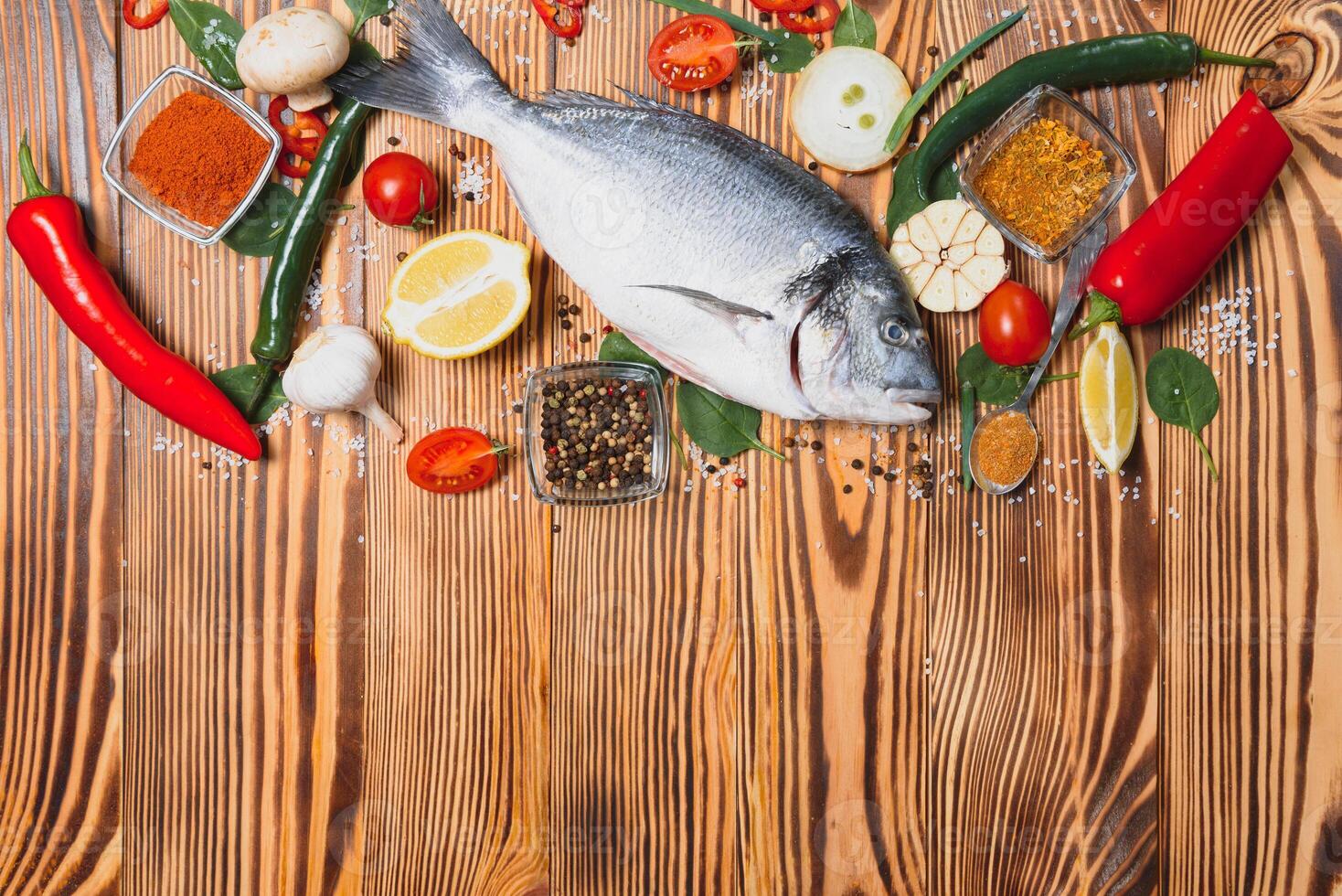 Fresh raw dorado fish on baking paper with lemon, pepper, tomatoes and various spices on wooden background with copy space photo