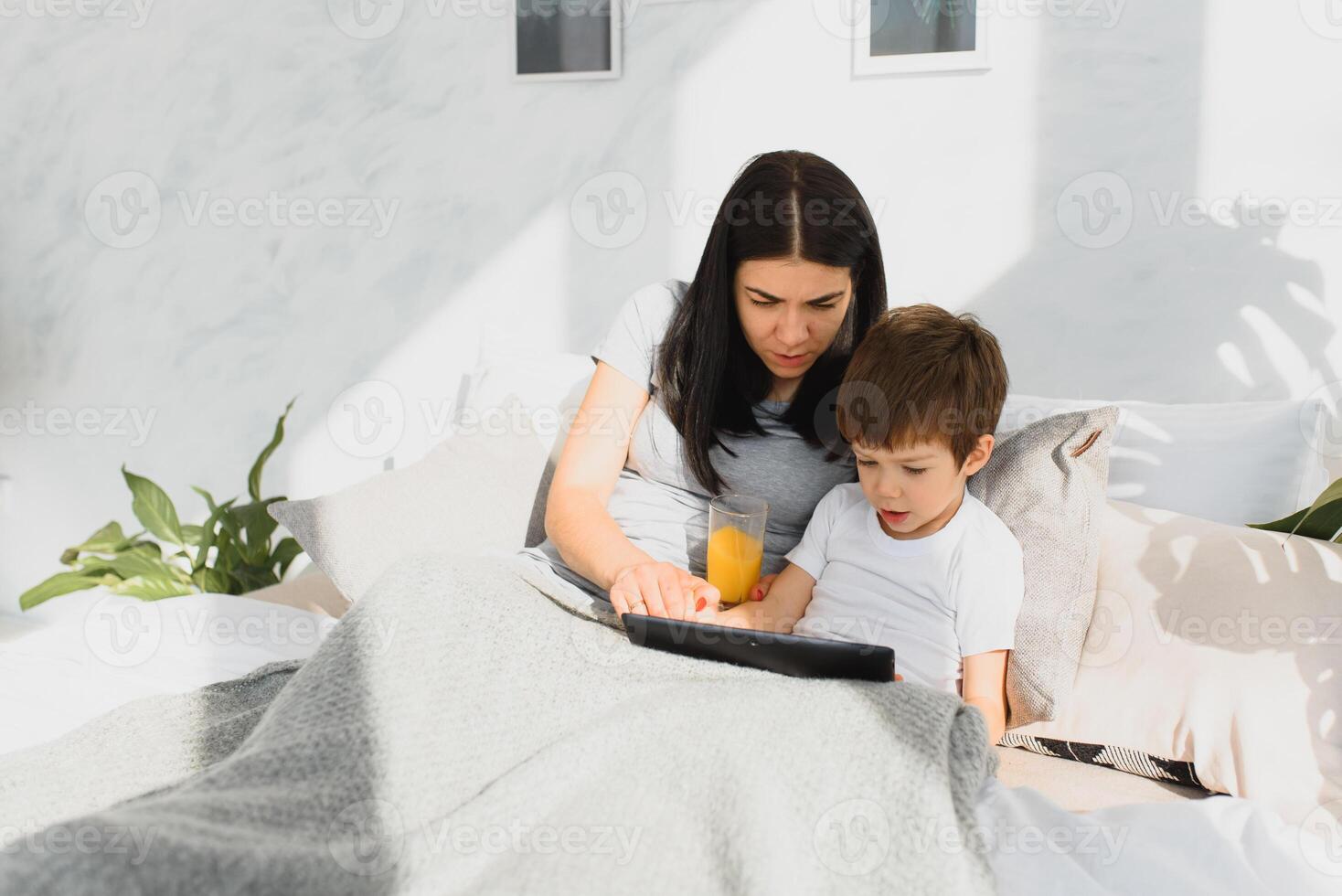 Beautiful smiling mother and son playing with digital tablet laying on bed. photo