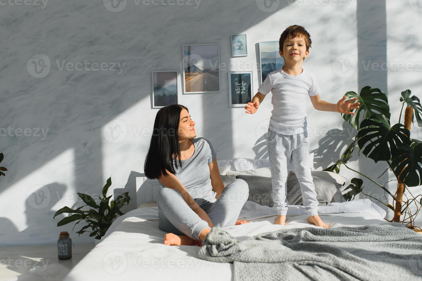 Mom playing with her child in the bedroom. Mother with son sharing good emotions while relaxing at home. Son jumping on the bed. photo