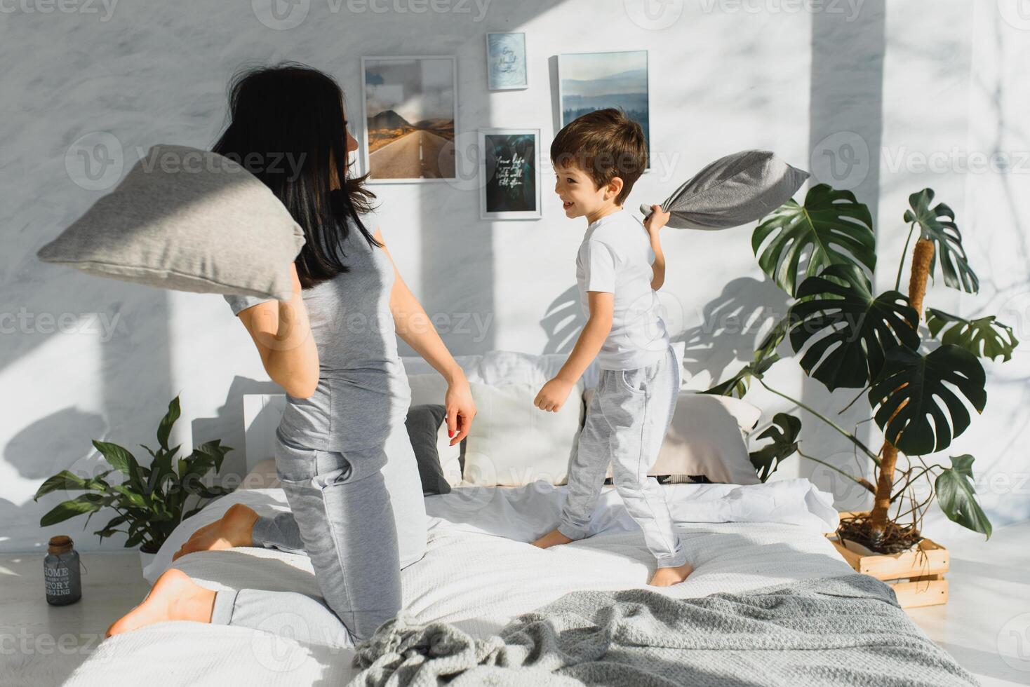Mommy and son laughing and playing on the bed, having a pillow fight in the morning while wearing pajamas. Family casual lifestyle series. photo