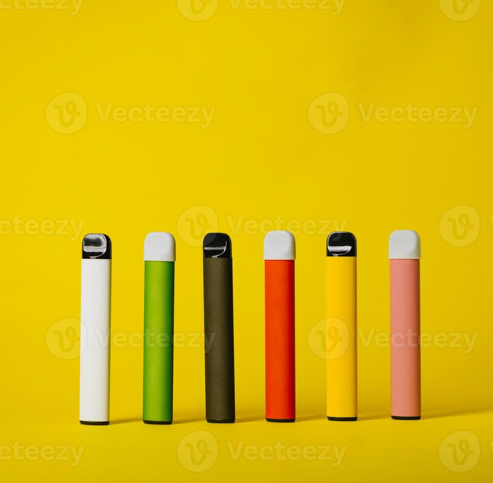 Set of colorful disposable electronic cigarettes with shadows on a yellow background. The concept of modern smoking, vaping and nicotine photo