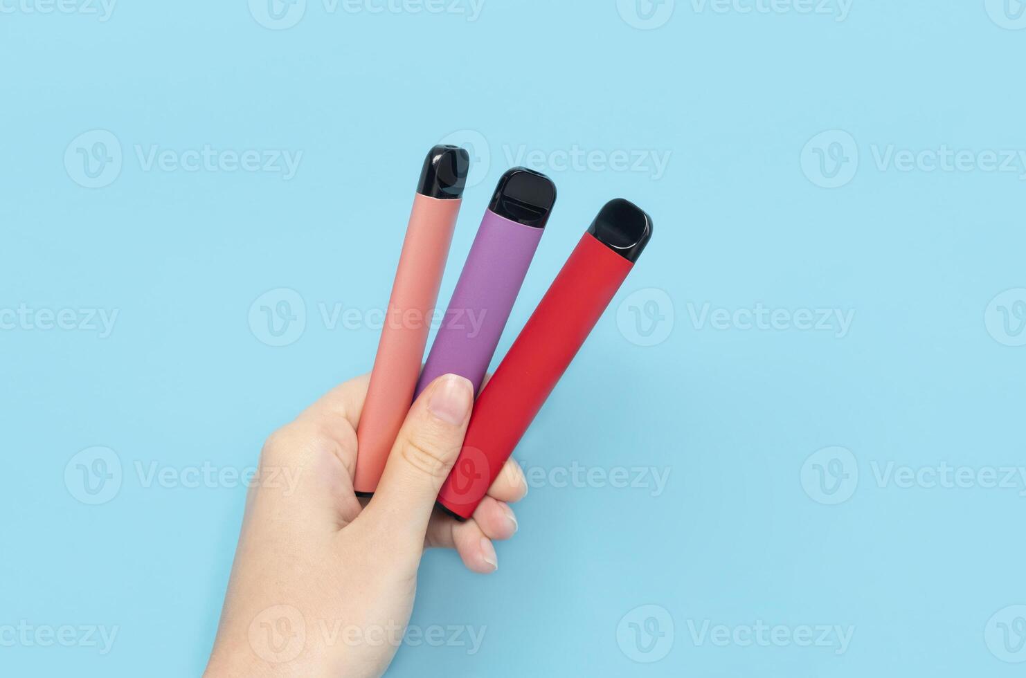 Disposable electronic cigarettes in hand closeup on a blue background. The concept of modern smoking, vaping and nicotine. Copy space photo