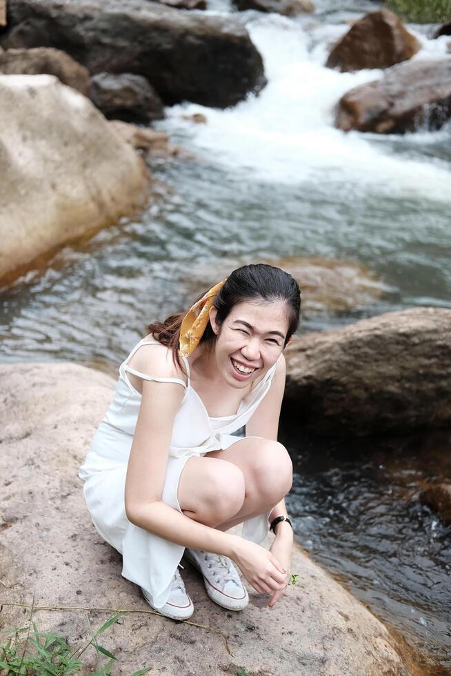 Smiling Asian woman sitting on the rocky in natural and stream in forest. photo