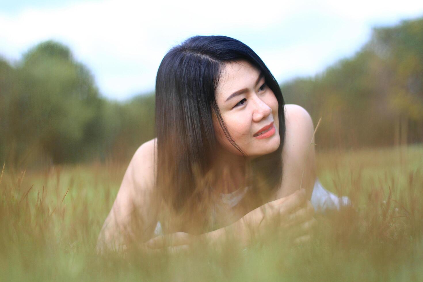 Beautiful asian woman in white dress relax and smiling on green field in natural park. Thai girl or Chinese Girl enjoy on holiday with sunlight in garden photo