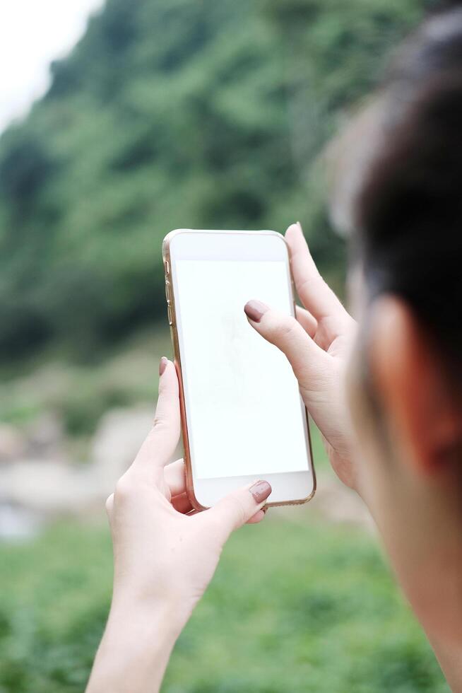Pretty Asian woman is holding smartphone for take a photo in tropical forest. Freedom life and techonology in nature Concept.