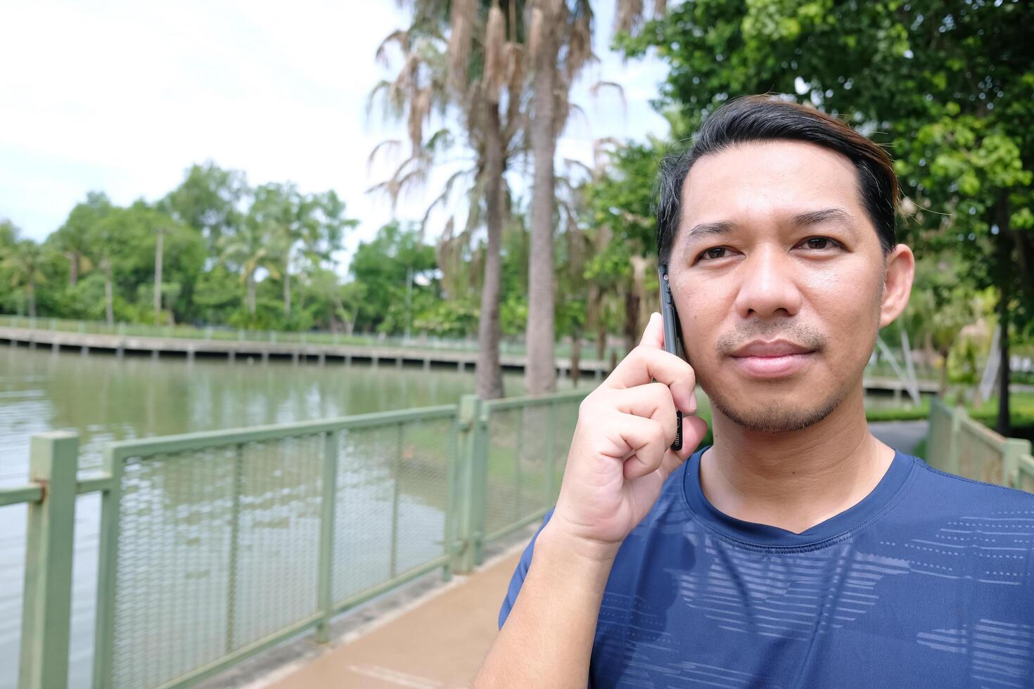 Smiling Asain man talking with smartphone in the park. Technology and lifestyle Concept photo